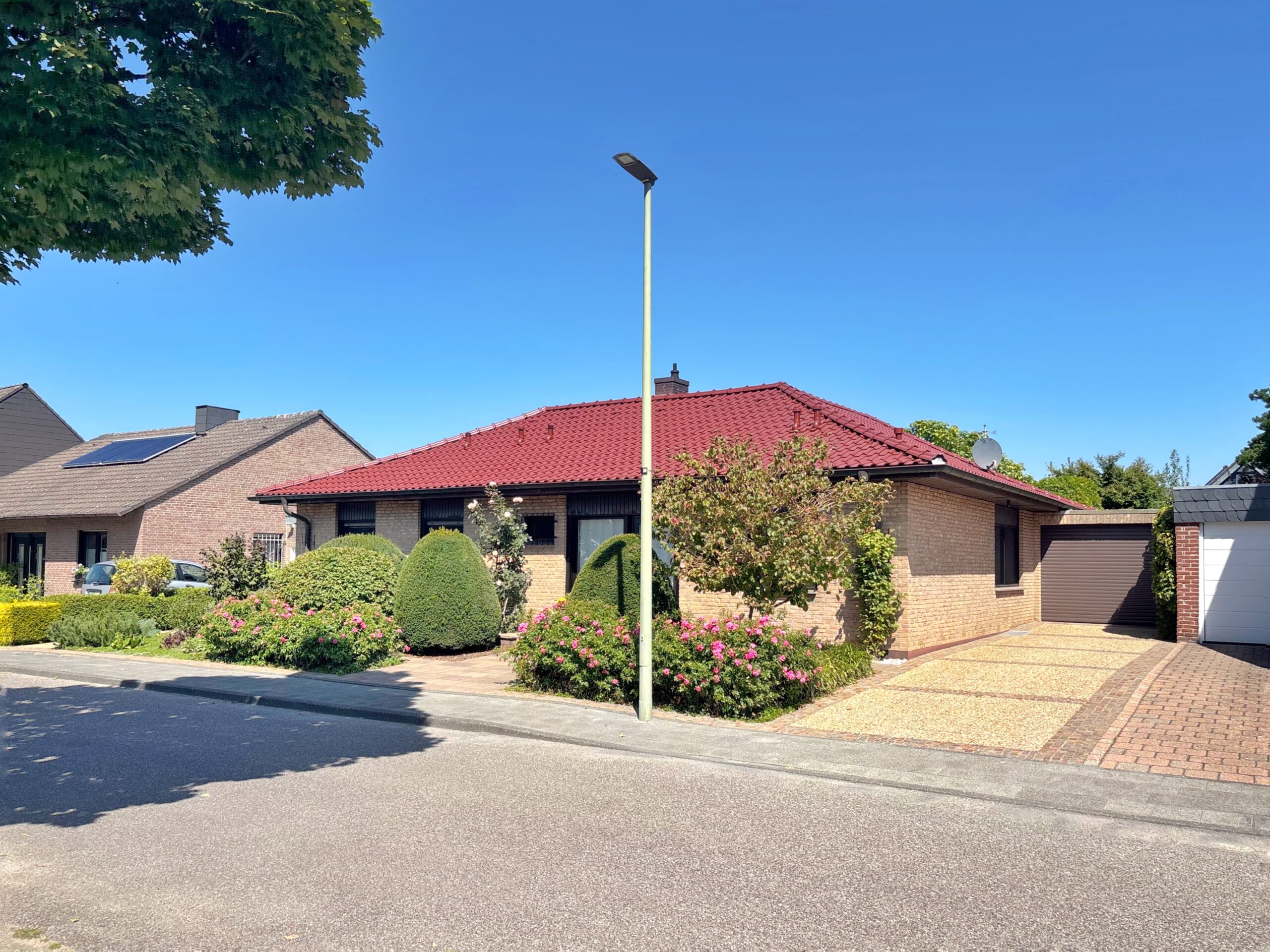 Das Bild zeigt ein Bungalow mit heller Fassade, rotem Dach und einem kleinen Vorgarten.