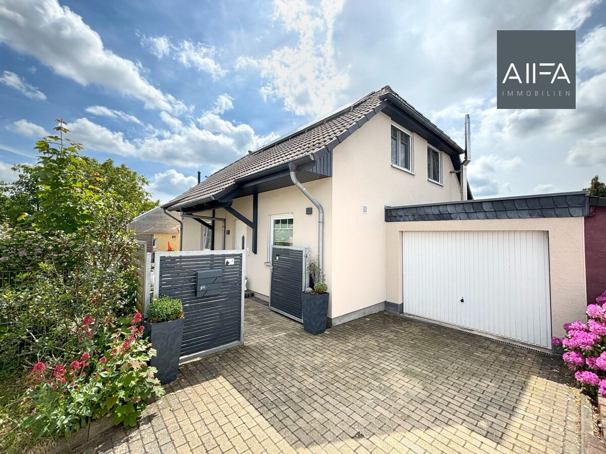 Das Bild zeigt die Außenansicht der hell verputzten Immobilie mit Einfahrt und Garage.