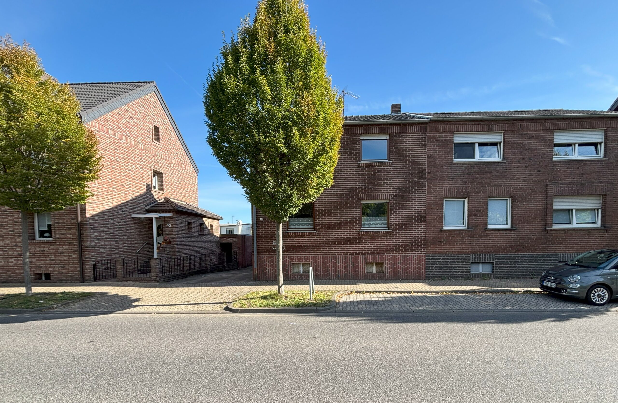 Das Bild zeig eine zweigeschossige Doppelhaushälfte mit rotem Klinkerstein. Eine Hauseinfahrt befindet sich auf der linken Seite.