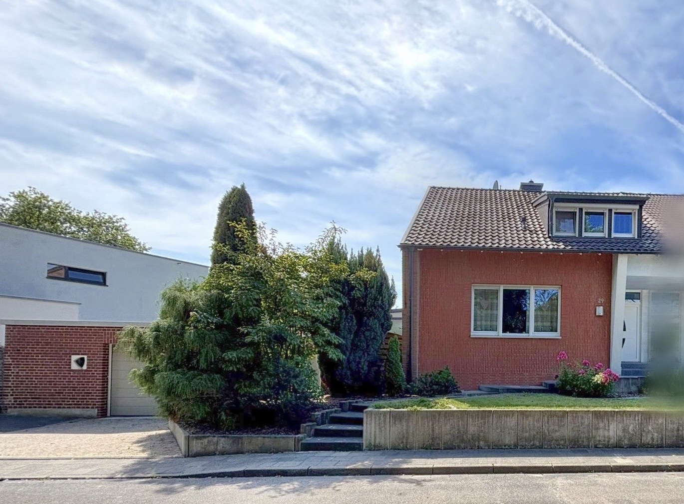 Das Bild zeigt eine Doppelhaushälfte. Im Vordergrund befindet sich eine kleine Mauer. Stufen führen zum Haus. Eine Garage ist links im Bild zu sehen.