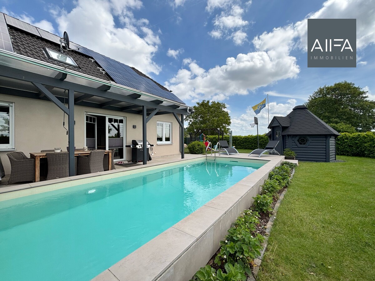 Das Foto zeigt die Rückseite eines Hauses mit Terrasse, Pool und Rasenfläche.